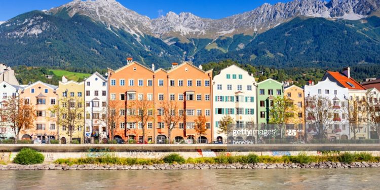 People walk and bike on the Inn River waterfront in downtown Innsbruck Tyrol Austria on a sunny day.