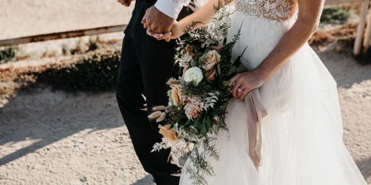 Close-up of bride and groom walking on path at the coast