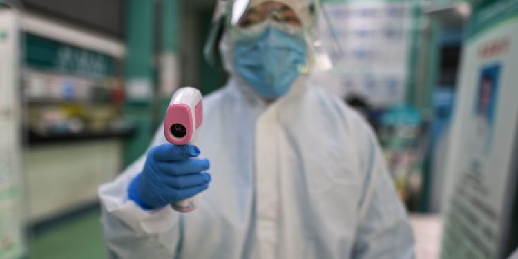 TOPSHOT - A medical worker prepares to check the temperature of an AFP photojournalist before a COVID-19 coronavirus test in Wuhan in China's central Hubei province on April 16, 2020. - China has largely brought the coronavirus under control within its borders since the outbreak first emerged in the city of Wuhan late last year. (Photo by Hector RETAMAL / AFP) (Photo by HECTOR RETAMAL/AFP via Getty Images)