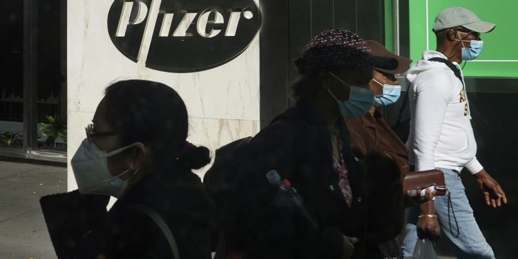 Pedestrians walk past Pfizer world headquarters in New York on Monday Nov. 9, 2020. Pfizer says an early peek at its vaccine data suggests the shots may be 90% effective at preventing COVID-19, but it doesn't mean a vaccine is imminent. (AP Photo/Bebeto Matthews)