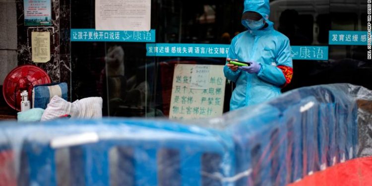 A community volunteer uses her mobile phone near a barrier separating a residential compound in Wuhan, China's central Hubei province on April 2, 2020. - Wuhan, the epicentre of the coronavirus pandemic, is very slowly re-emerging from more than two months of demoralising lockdown. But endless rows of plastic yellow or blue barriers now run along streets throughout the city of 11 million people, just one indication of how life for its traumatised residents remains severely disrupted. (Photo by NOEL CELIS / AFP) (Photo by NOEL CELIS/AFP via Getty Images)