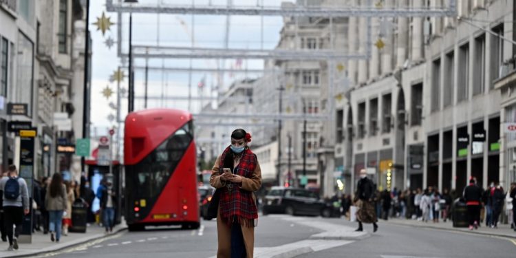 A woman wearing a protective face covering checks her phone as she walks down the centre of Oxford Street in London, on October 17, 2020, as Londoners face more stringent novel coronavirus COVID-19 restrictions as the number of cases rises. - The government has announced that London has moved into tier two, the high alert level, of a three tier system of restrictions. (Photo by JUSTIN TALLIS / AFP)