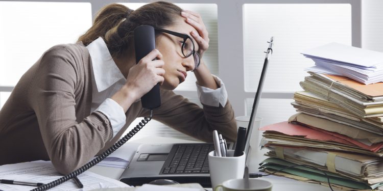 A stressed business woman looks tired  she answer telephones in her office