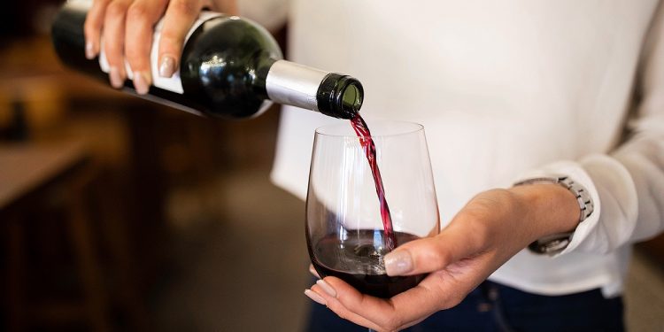 Close-up of a woman hand pouring wine into a glass. Female waiter serving red wine in a winery.