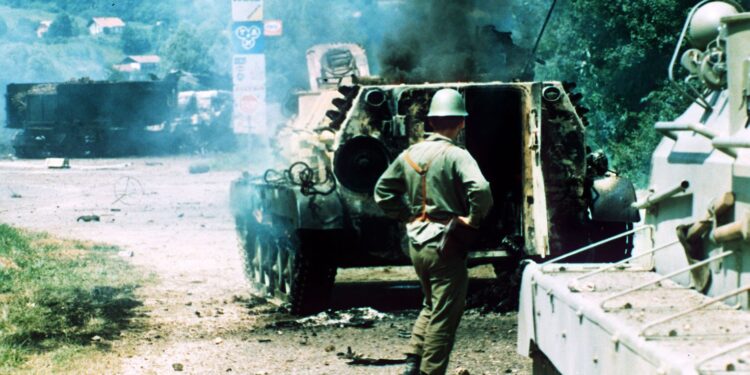 Destroyed amored car by Slovene Defence Forces. A soldier of the Yugoslav army stands by a smoking armored car after a firefight with members of the Slovene Devence Forces in Brezice, about 15 miles (25 Kilometers) from Zagreb, Tuesday. Yugoslav army are on monoever in area of independence movement in Slaovenia. (AP-Photo/Michel Eular) 2.7.1991