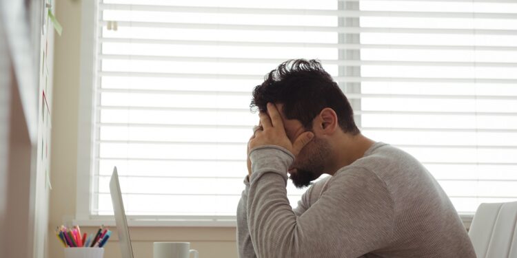 Stressed man sitting with hands on head at home