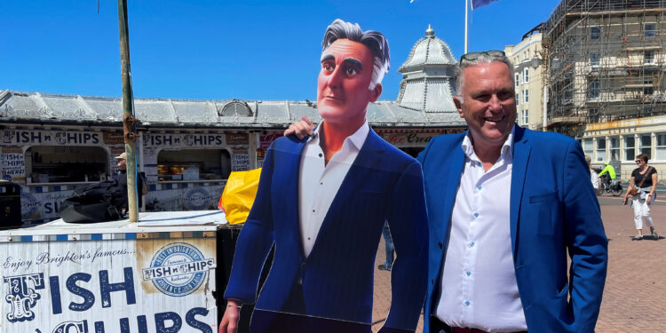 Steve Endacott, an independent candidate in the Brighton Pavilion race, poses with his AI avatar outside Brighton pier in southern Britain, June 17, 2024. REUTERS/Muvija M