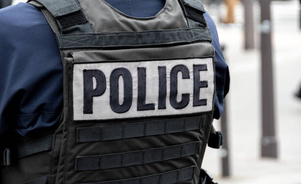 Close-up 'POLICE' marking written on the back of a bulletproof vest worn by a French police officer on a street in Paris, France. Concepts of law enforcement, crime, delinquency and criminal affairs