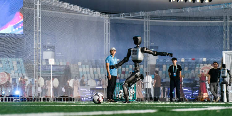 A Booster T2 robot practises striking a football ahead of the opening of the World Humanoid Robot Games in Beijing, China, on Friday, Aug. 21, 2026. The World Humanoid Robot Games will run through Aug. 26. Photographer: Qilai Shen/Bloomberg
